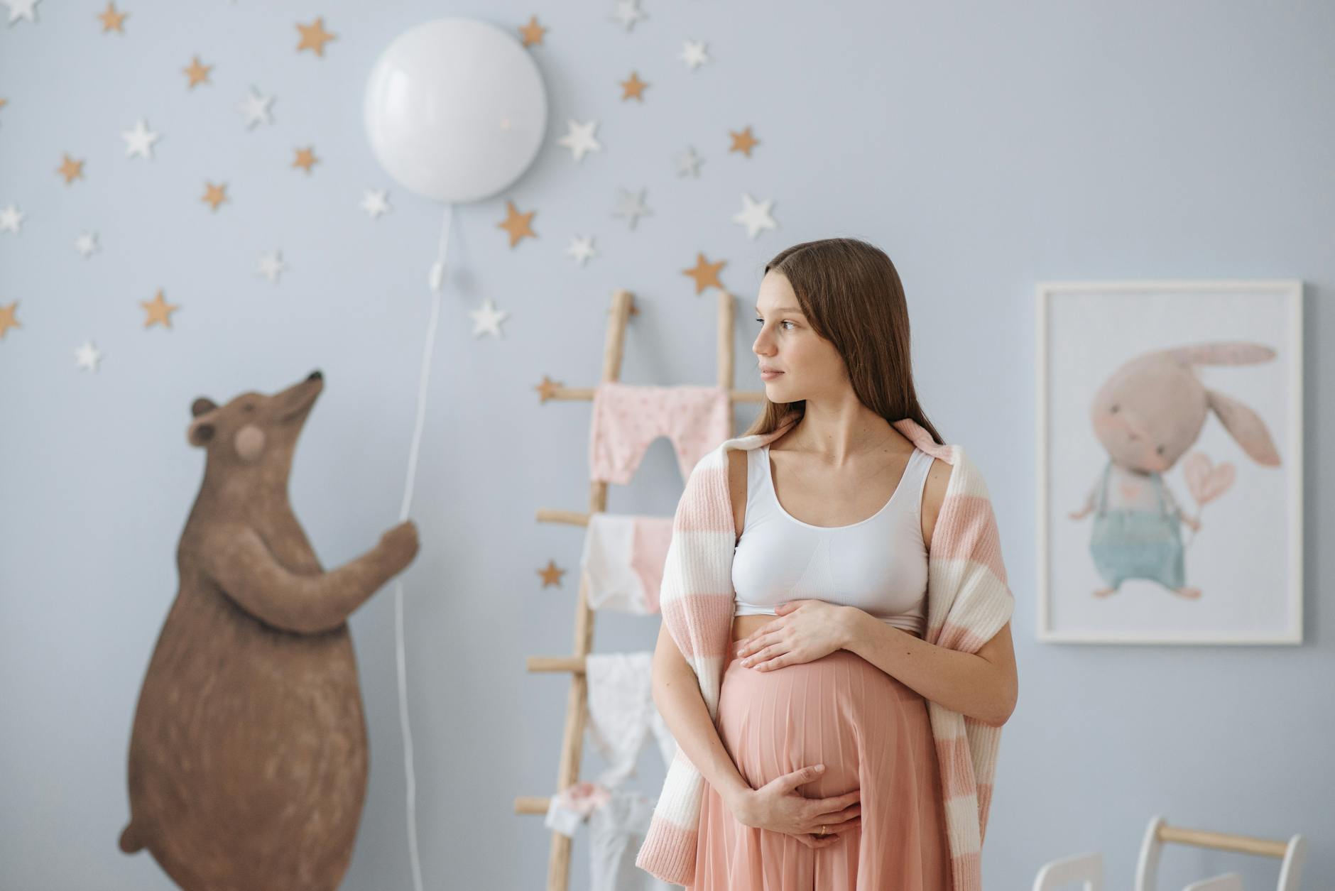 A beautiful pregnant woman in a stylish baby room, holding her belly. [pexels]