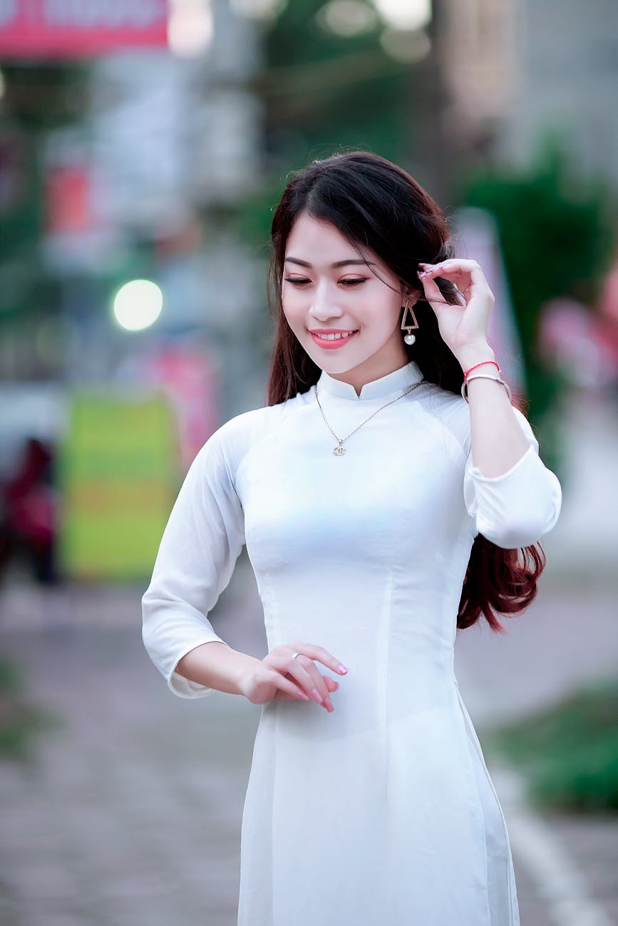 A woman in a white Ao Dai poses gracefully outdoors, showcasing traditional Vietnamese fashion. [pexels]