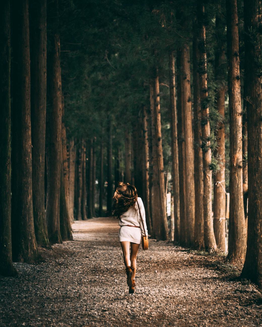 A woman walks along a serene tree-lined path, embracing freedom and nature. [pexels]