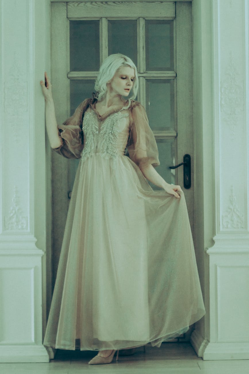 A woman wearing a luxurious vintage ball gown stands elegantly by a doorway. [pexels]