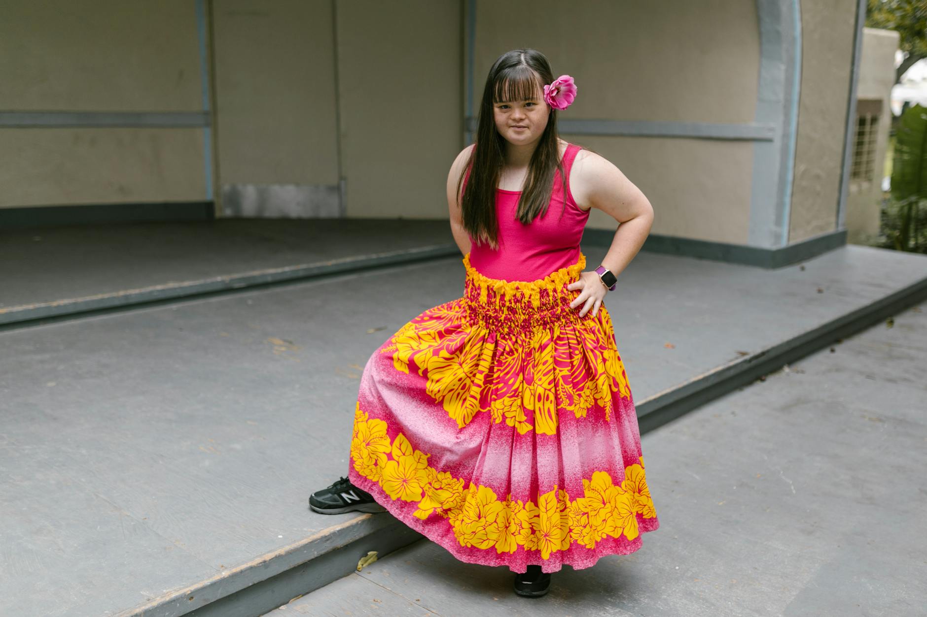 A young woman with Down syndrome poses confidently in a vibrant Hawaiian dress. [pexels]