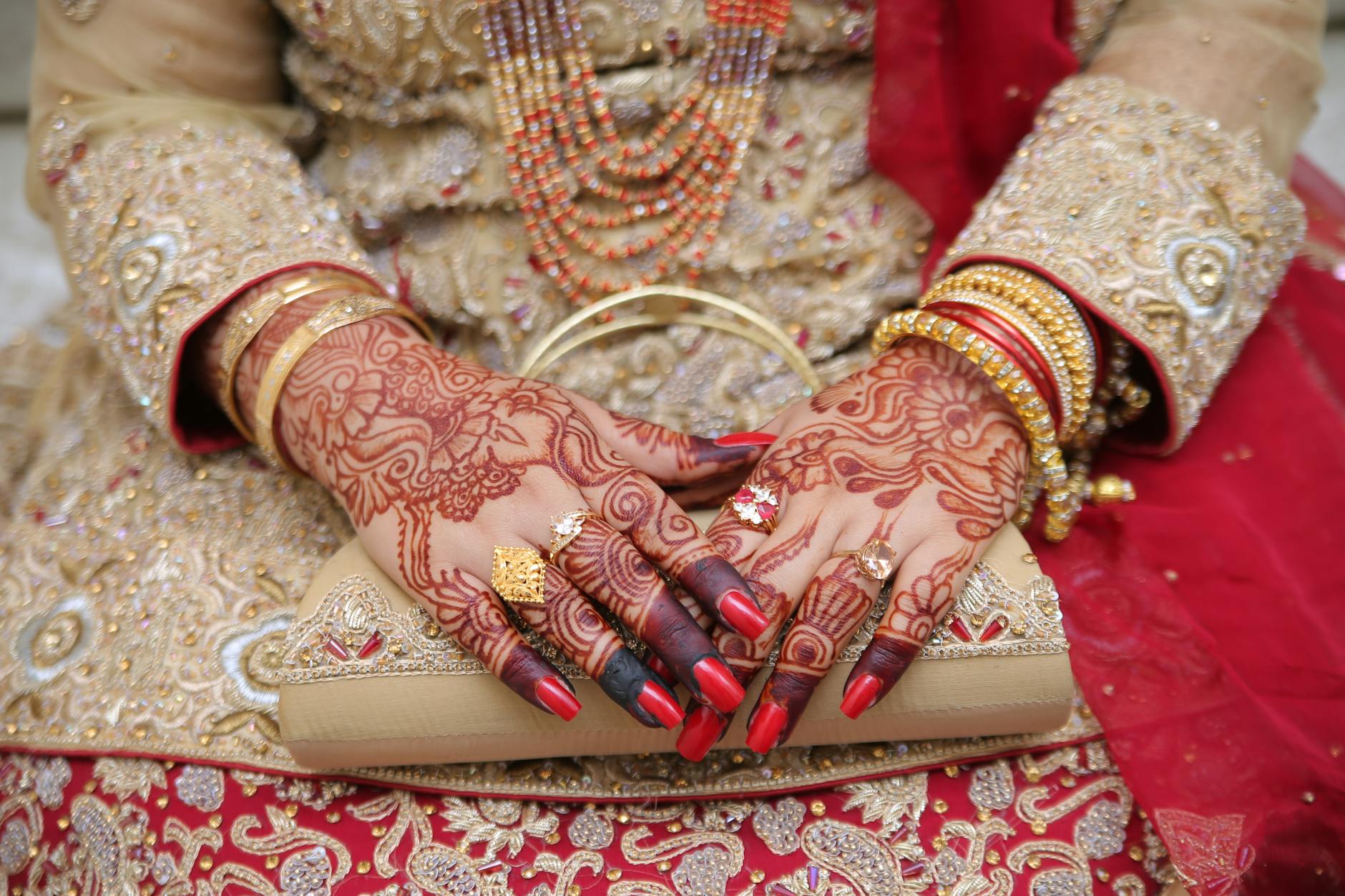 Close-up of an Indian bride's hands adorned with mehndi, jewelry, and traditional attire. [pexels]