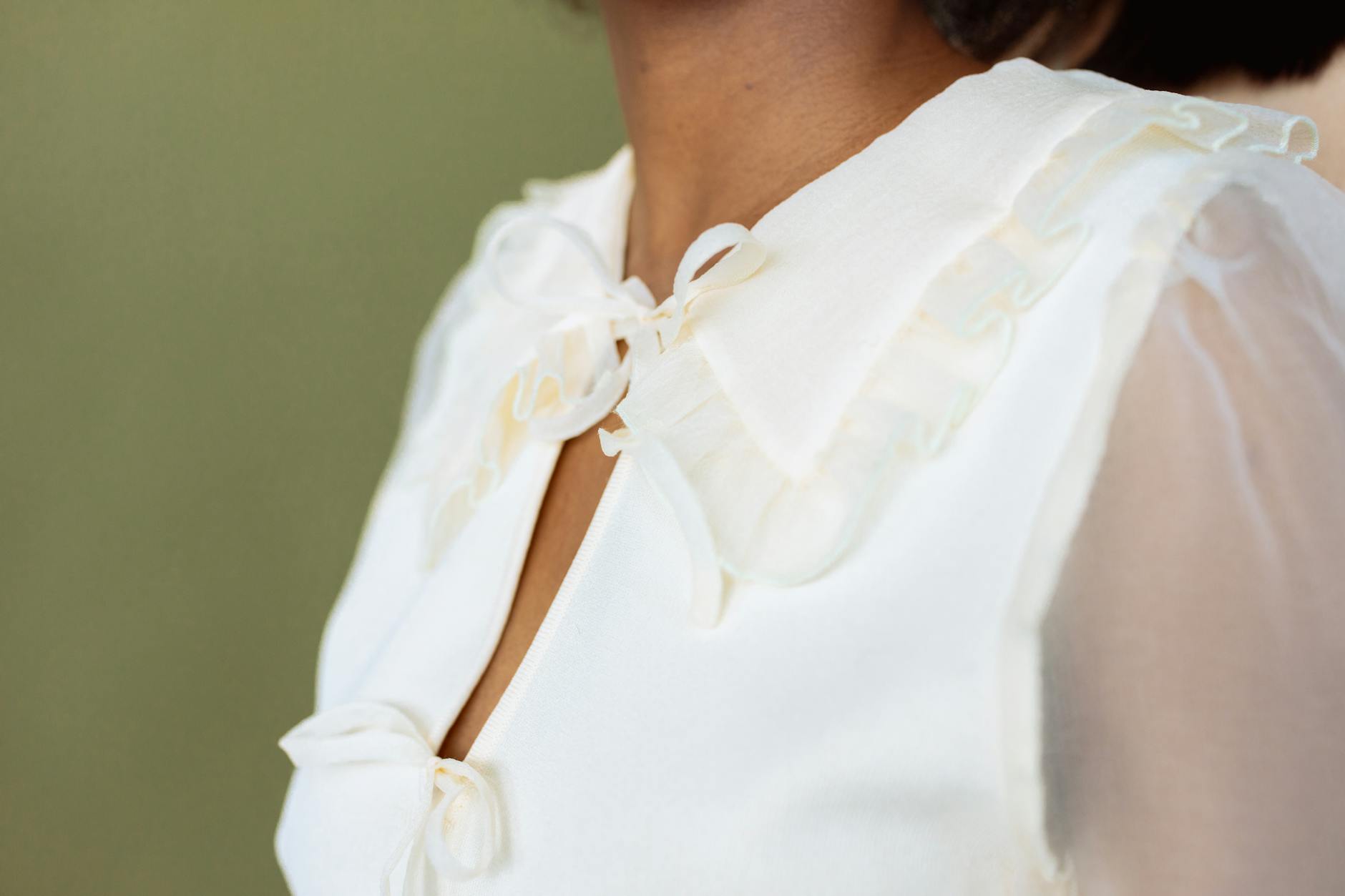 Close view of a person wearing an elegant white blouse with a delicate ribbon detail. [pexels]