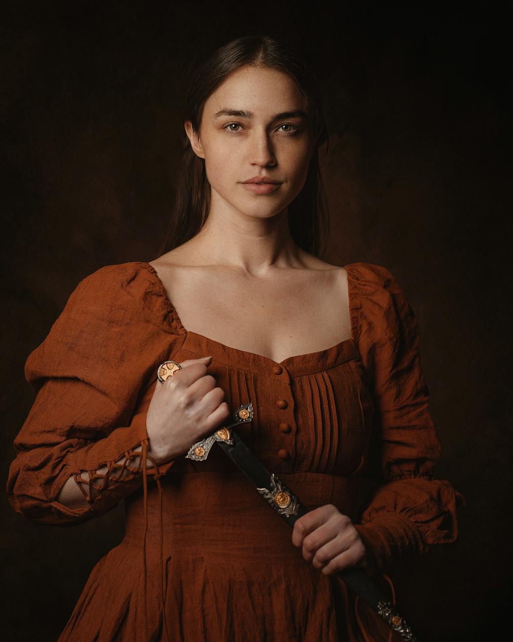 Elegant studio portrait of a woman in a medieval gown holding a dagger. [pexels]