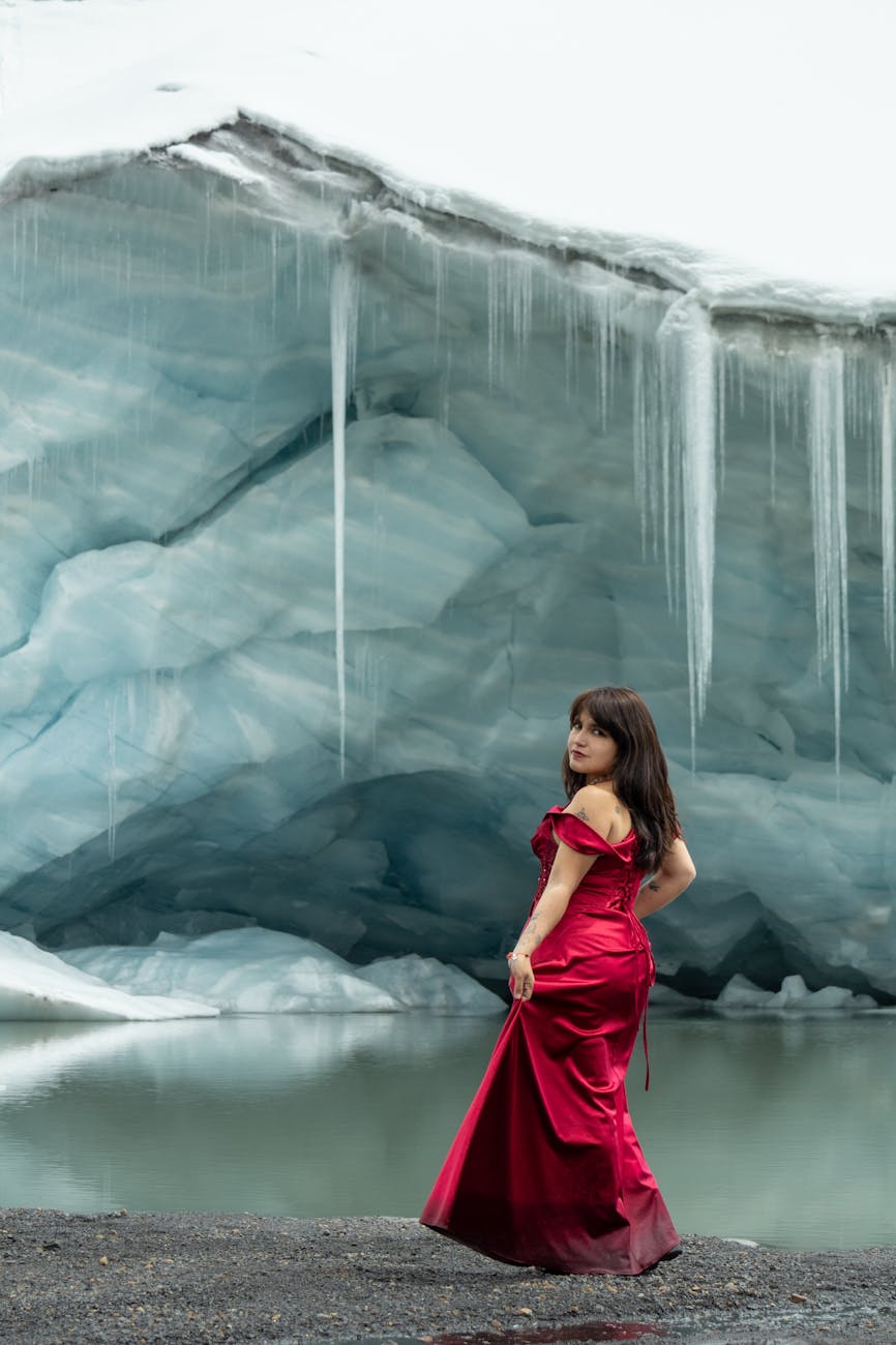 Elegant woman in a red dress standing by a tranquil glacier lake. [pexels]