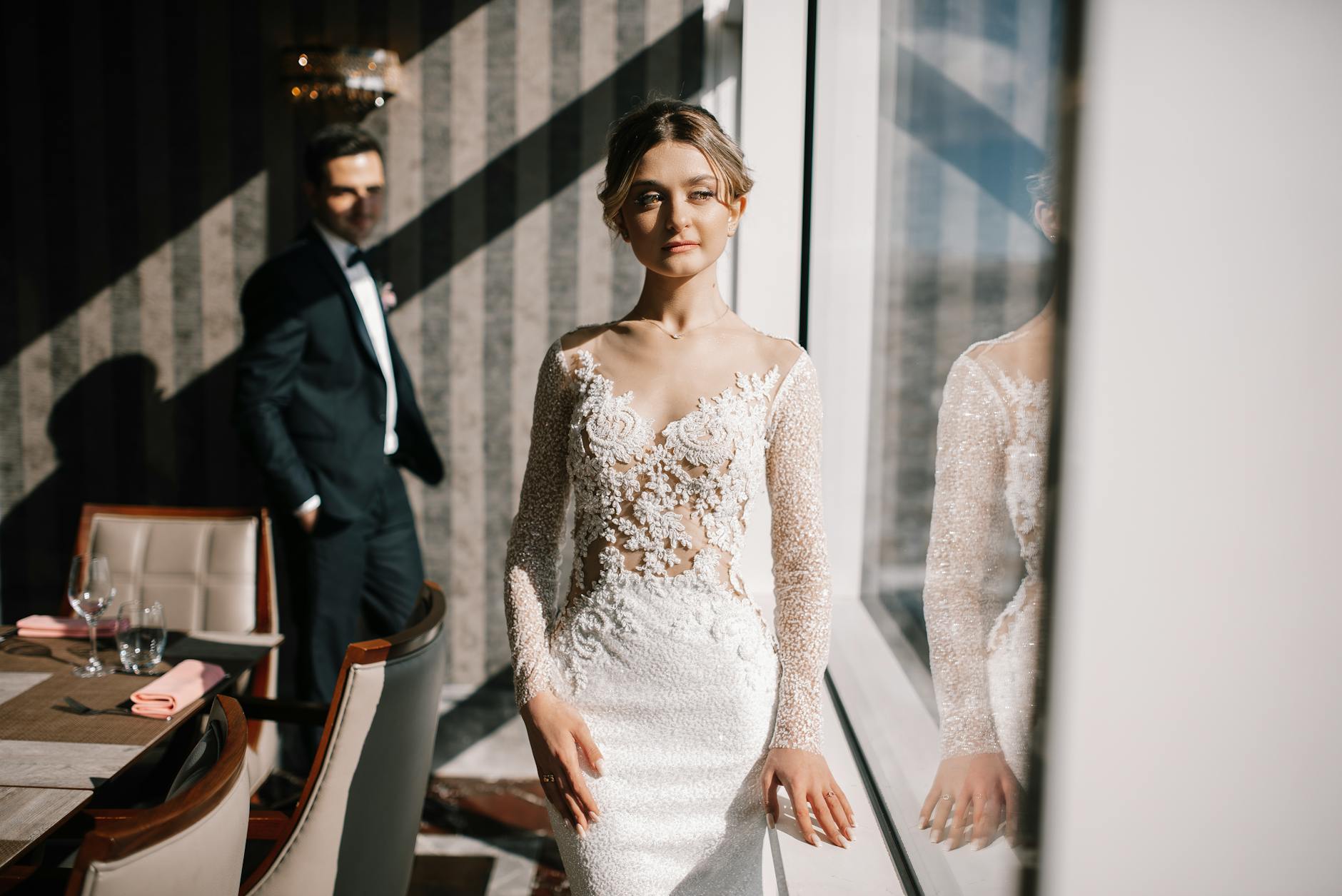 Romantic indoor wedding photoshoot displaying the bride in an elegant gown with groom in background. [pexels]