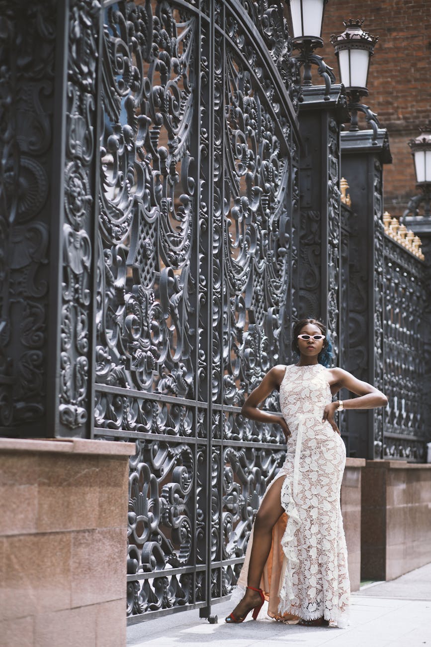 Stylish woman in an evening dress posing by a decorative iron gate outdoors. [pexels]