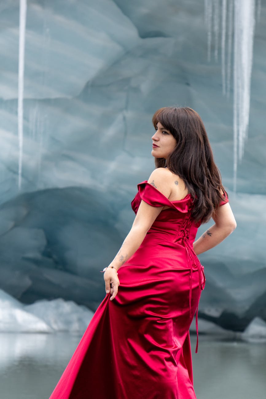 Woman in a vibrant red dress standing against a dramatic icy landscape. [pexels]
