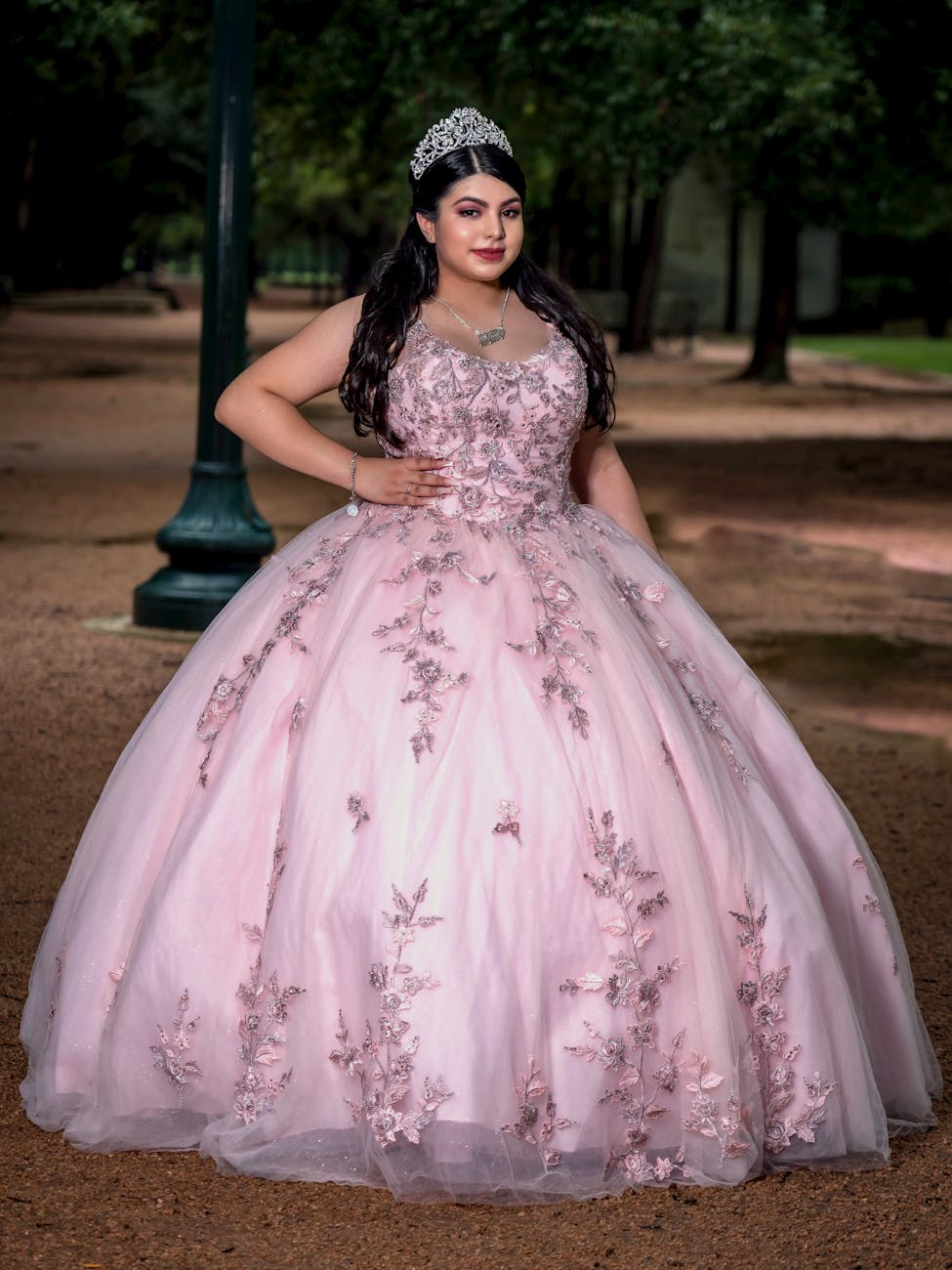 Young woman in a pink quinceañera dress poses elegantly outdoors. [pexels]
